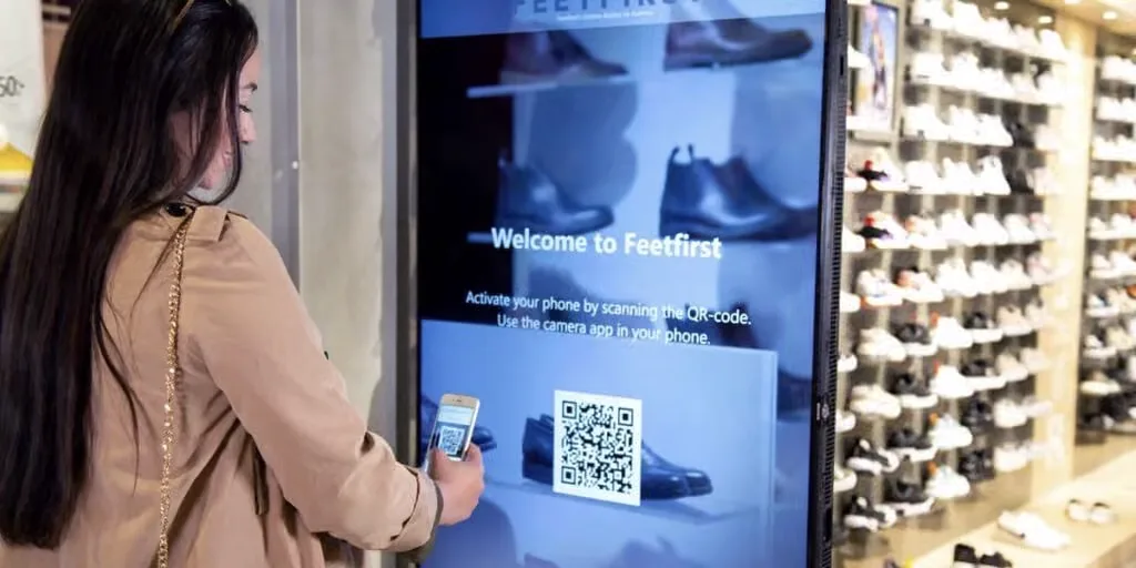Clienta escaneando con el móvil el código QR de una pantalla en una zapatería