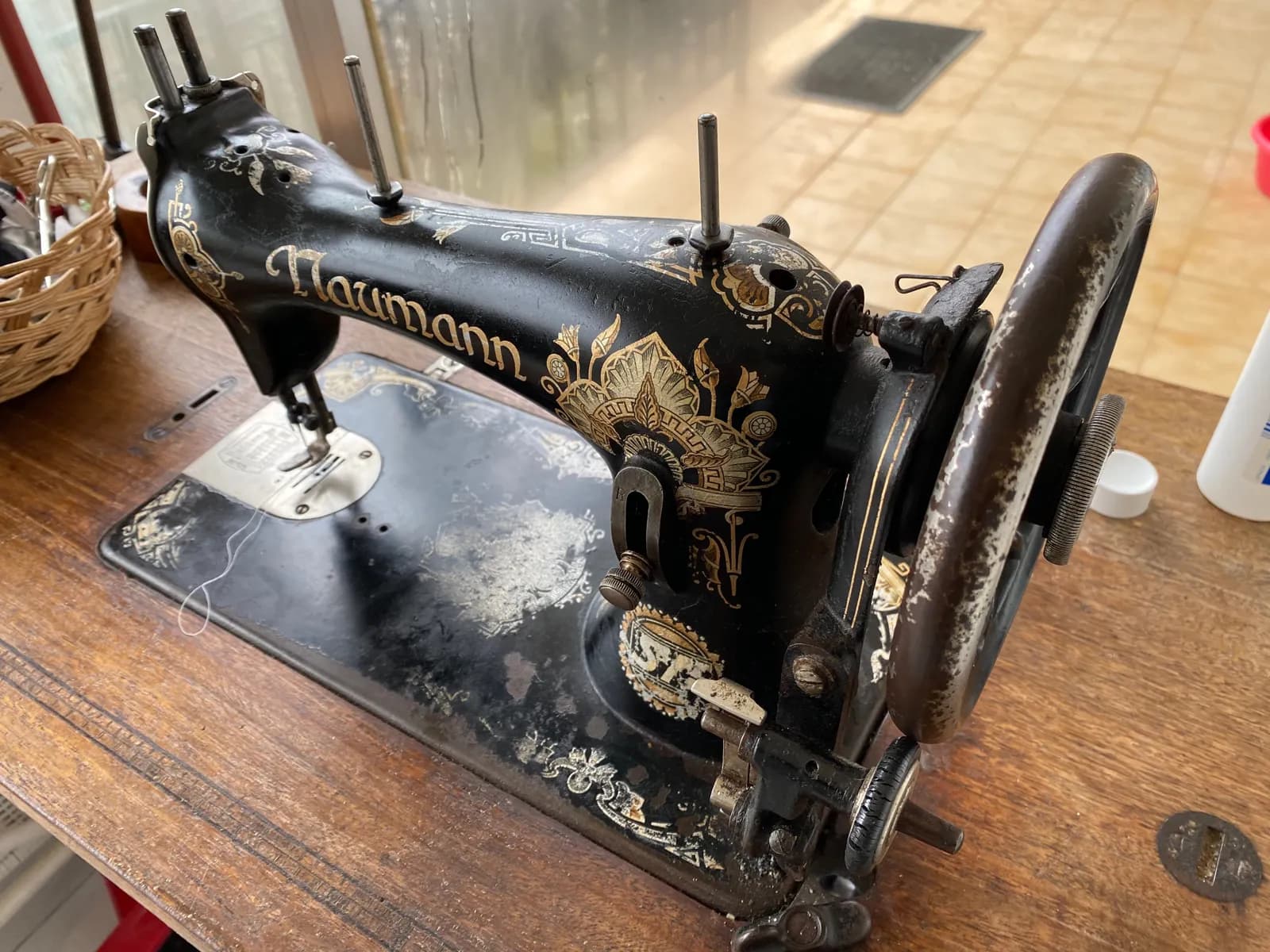 Máquina de coser antigua Naumann, negra con decoración dorada, sobre una mesa de madera