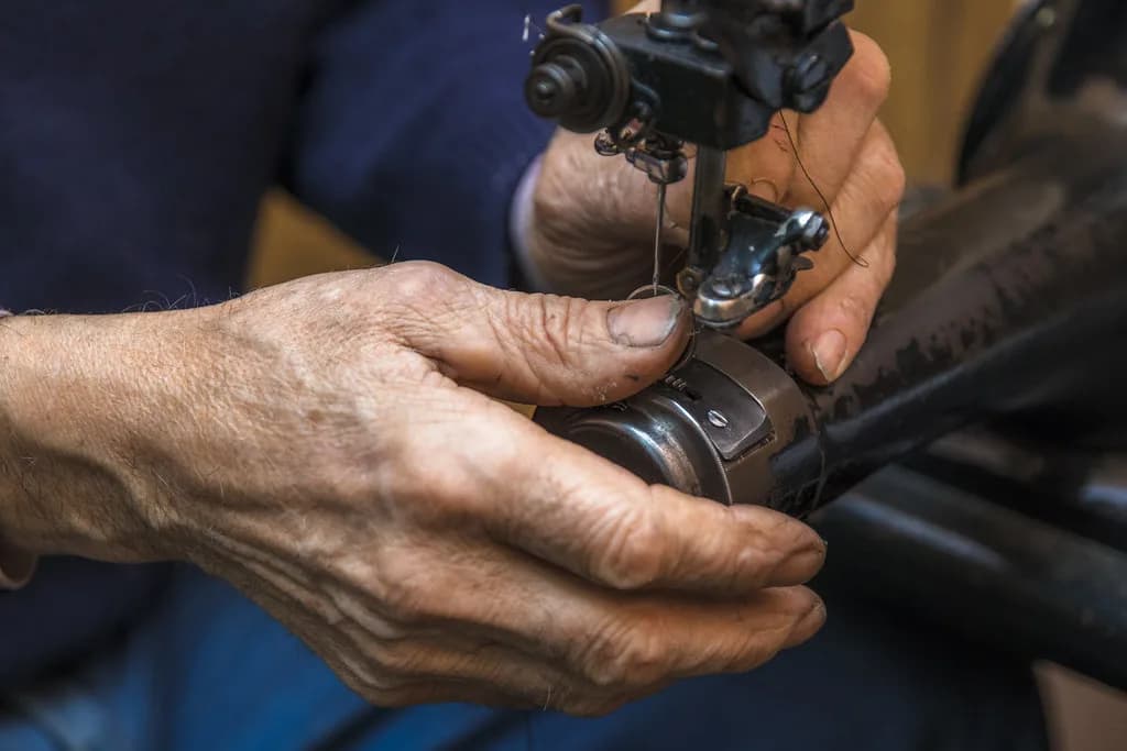 Manos de un sastre enhebrando la aguja de una máquina de coser antigua